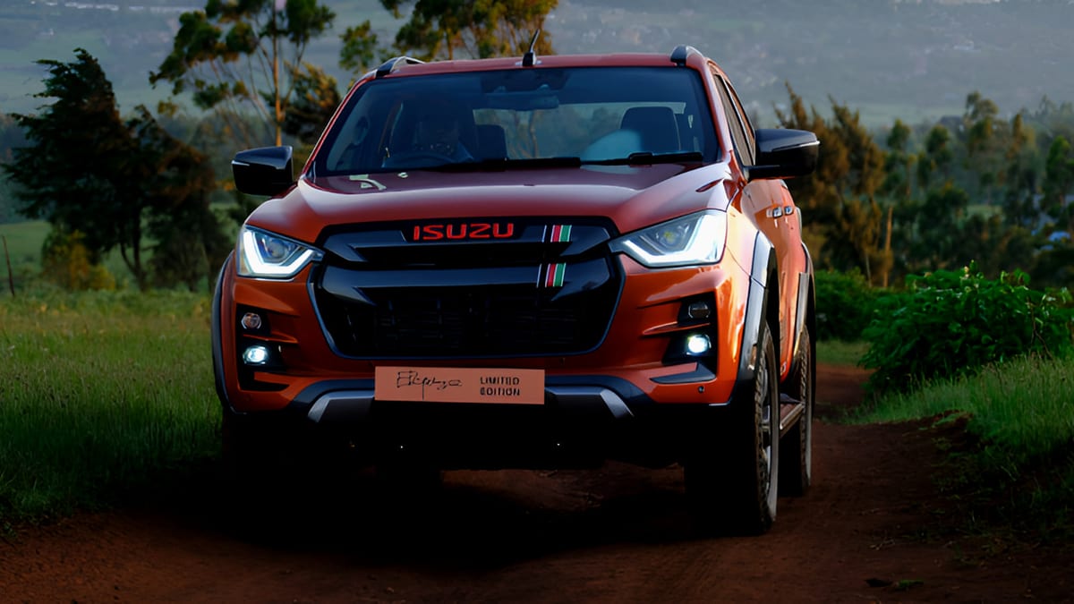 Isuzu D-Max Kipchoge 159 Limited Edition in desert orange, front three-quarter view, photographed on a grass track with hills behind.