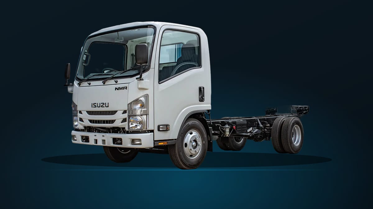 Isuzu NMR85H cab chassis, front three-quarter view on a dark studio ground, showing the bare frame rails behind the cab where a body is fitted.